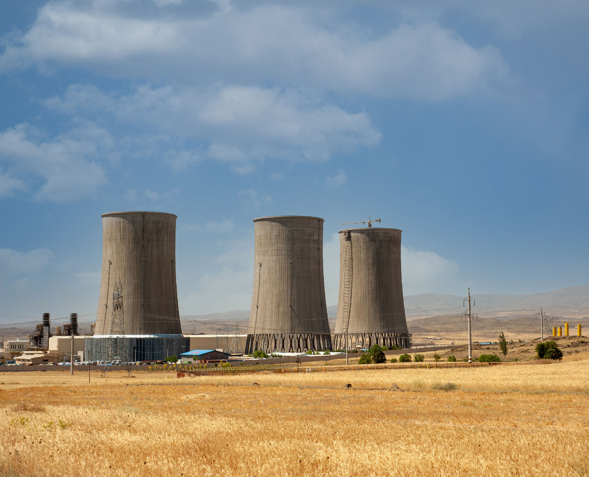 Nuclear power plant cooling towers, big chimneys beside Wheat field with partly cloudy sky in Kurdistan province, Iran